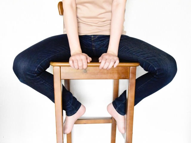 椅子に座って開脚をしている人物の体幹と下半身。股関節の柔軟性が全身の健康と連動していることを示すイメージ。